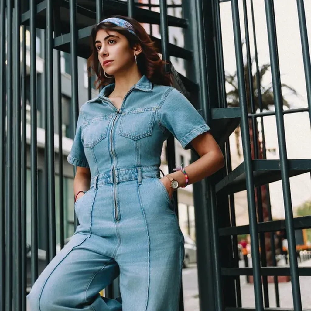 Woman in a denim utility jumpsuit with belt, practical chic 80s one-piece outfit