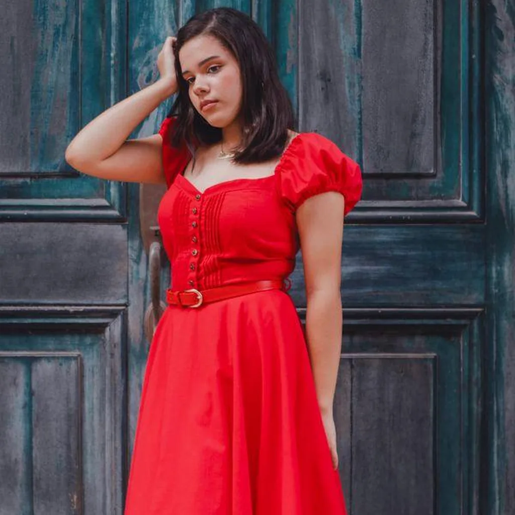 Woman in a red dress with wide belt and puff sleeves in front of a teal door, bold 80s outfit